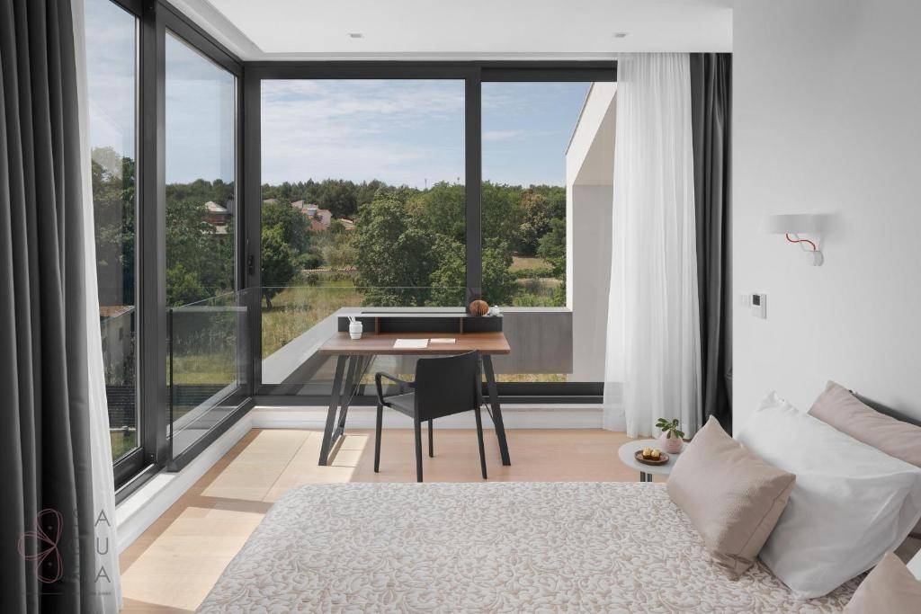 Helles Schlafzimmer mit raumhohen Fenstern, Schreibtisch und weitem Blick ins Grüne.