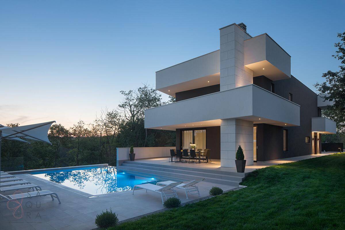 Elegantes modernes Haus mit Infinity-Pool und großer Terrasse, umgeben von üppiger Natur bei Sonnenuntergang.