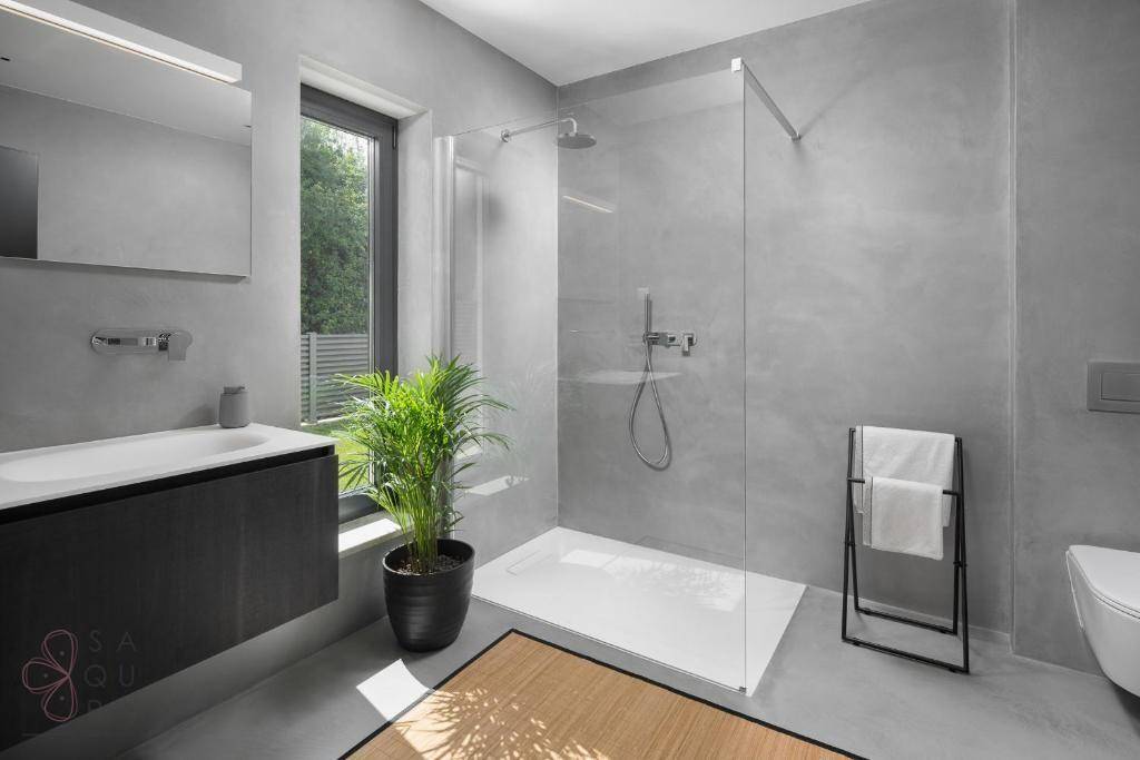Modernes Badezimmer in Grau mit ebenerdiger Dusche, Fenster und Pflanzenakzent.