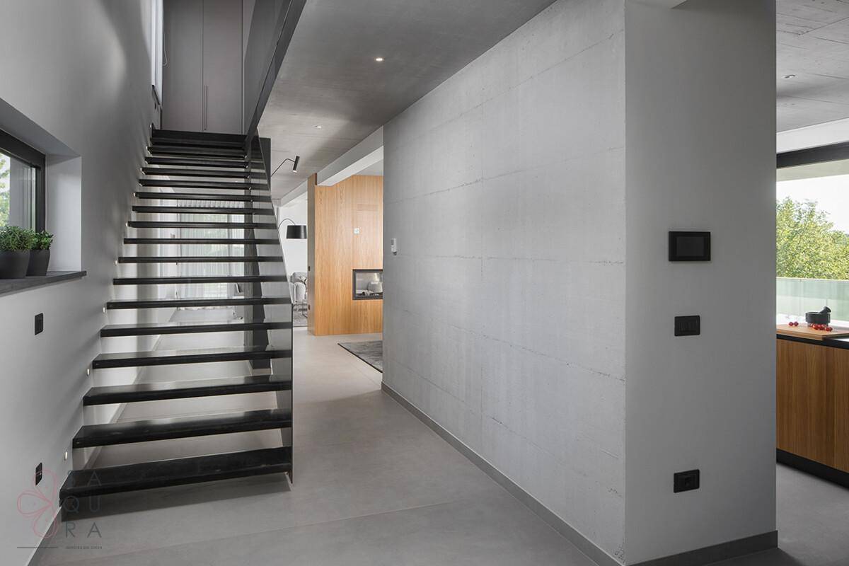 Heller Flur mit moderner Treppe, Betonwänden und Zugang zu verschiedenen Wohnbereichen.
