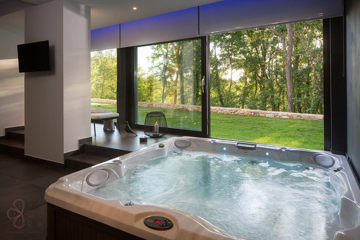 Entspannungsbereich mit Whirlpool und großen Panoramafenstern mit Blick in den Garten.