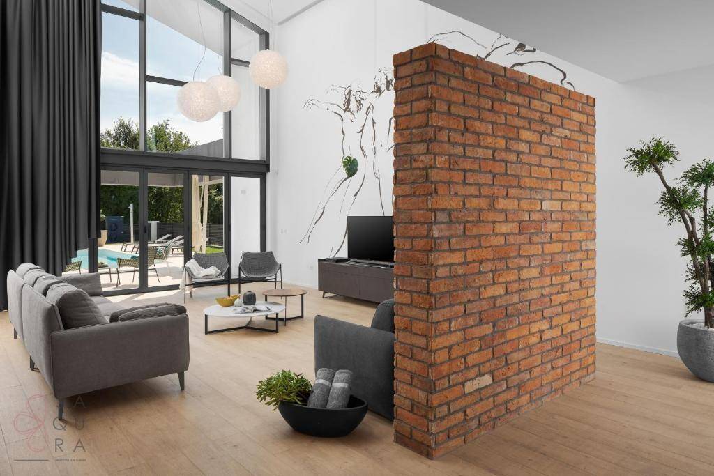 Modernes Wohnzimmer mit freistehender Ziegelwand, Holzboden und Blick ins Grüne.