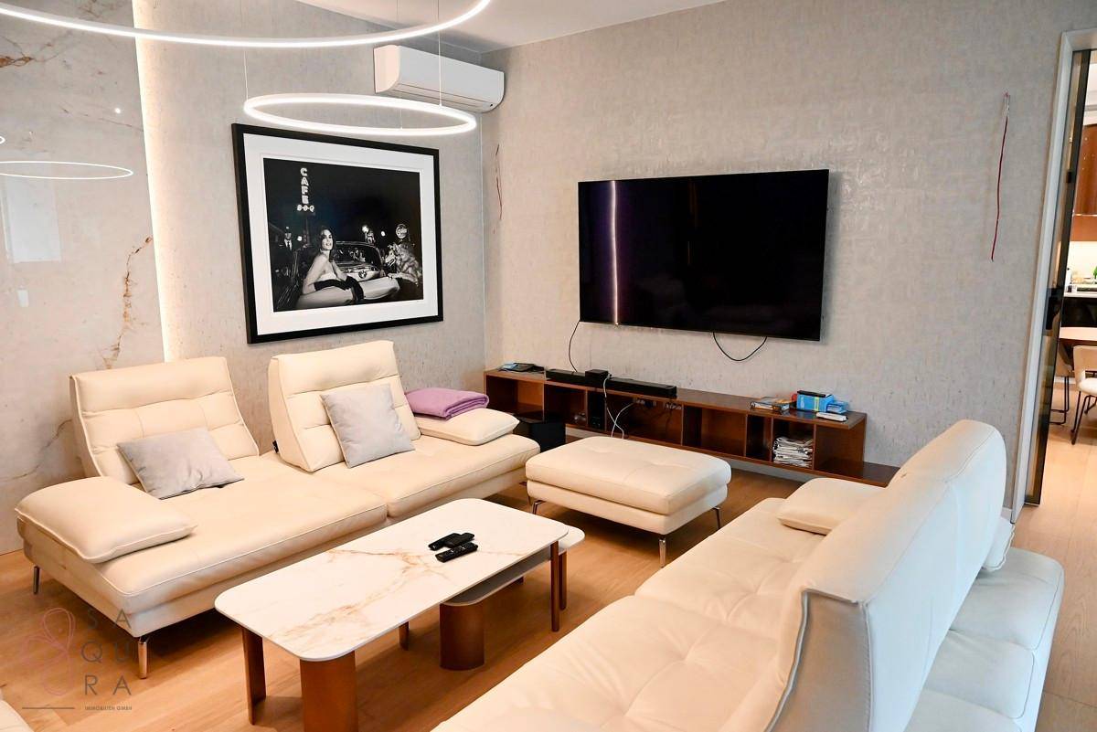 Modern eingerichtetes Wohnzimmer mit beigem Sofa, Wandfernseher und Klimaanlage.