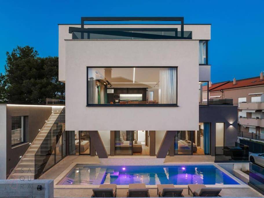Frontansicht der modernen Villa mit beleuchtetem Pool und großen Fensterfronten.