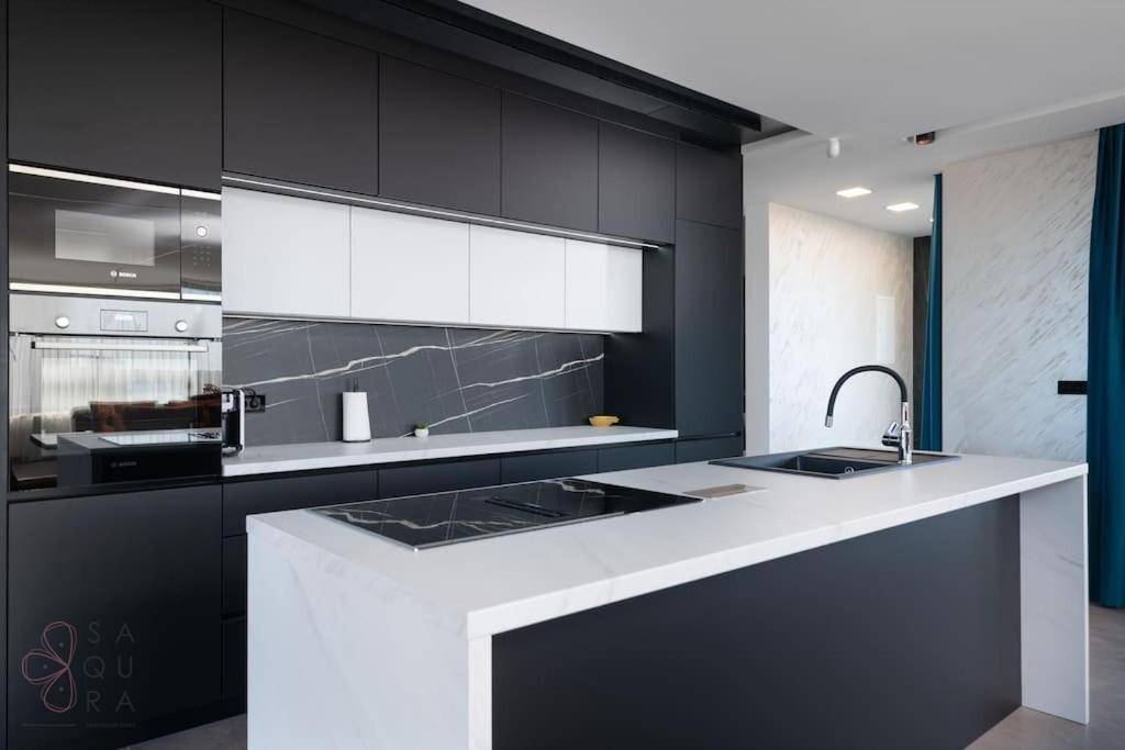 Moderne Küche mit dunklen Schränken, weißer Kücheninsel und Marmor-Rückwand, ausgestattet mit modernen Geräten.