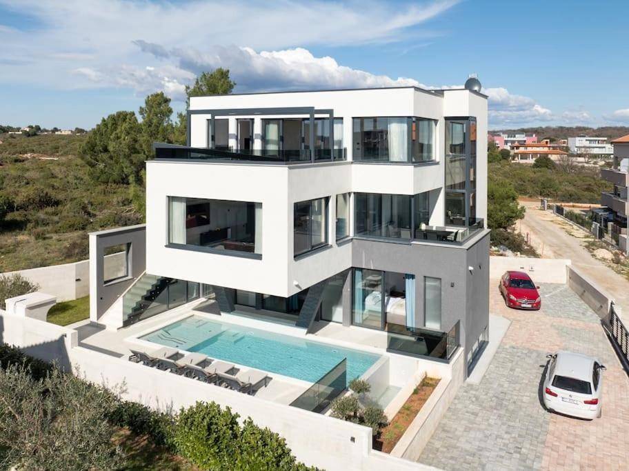 Moderne Villa mit Pool, gepflegtem Garten und Parkplätzen unter strahlendem Himmel.