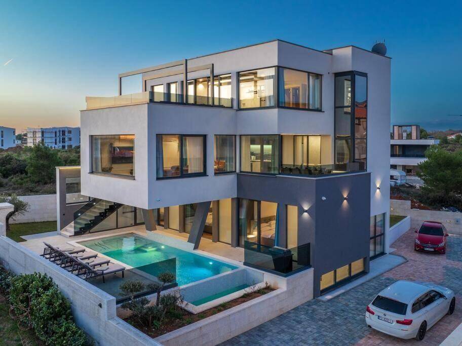 Elegante Villa bei Sonnenuntergang mit Pool, Liegestühlen und gepflasterter Auffahrt.