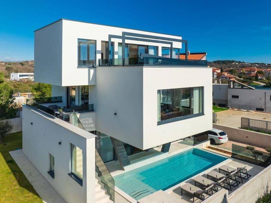 Moderne Villa mit klaren Linien, großem Poolbereich und Sonnenliegen unter blauem Himmel.