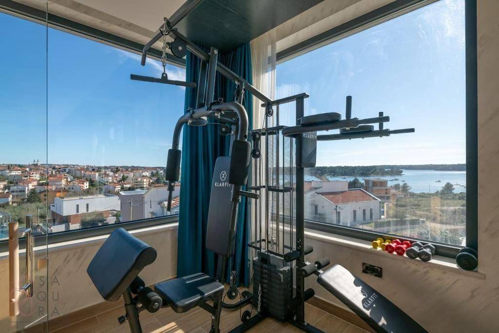 Fitnessraum mit Trainingsgeräten und großen Fenstern, die einen weiten Blick auf das Meer bieten.