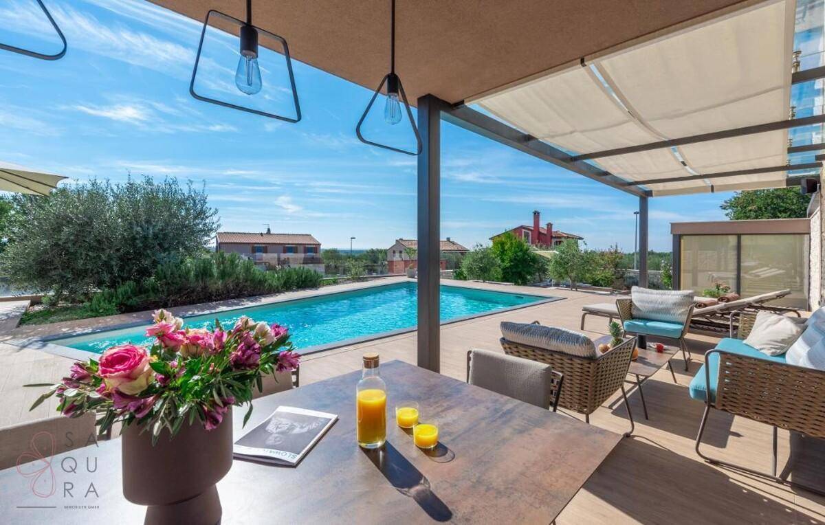 Sonnige Terrasse mit Esstisch, Blumen und Blick auf den Pool und die umliegende Landschaft.