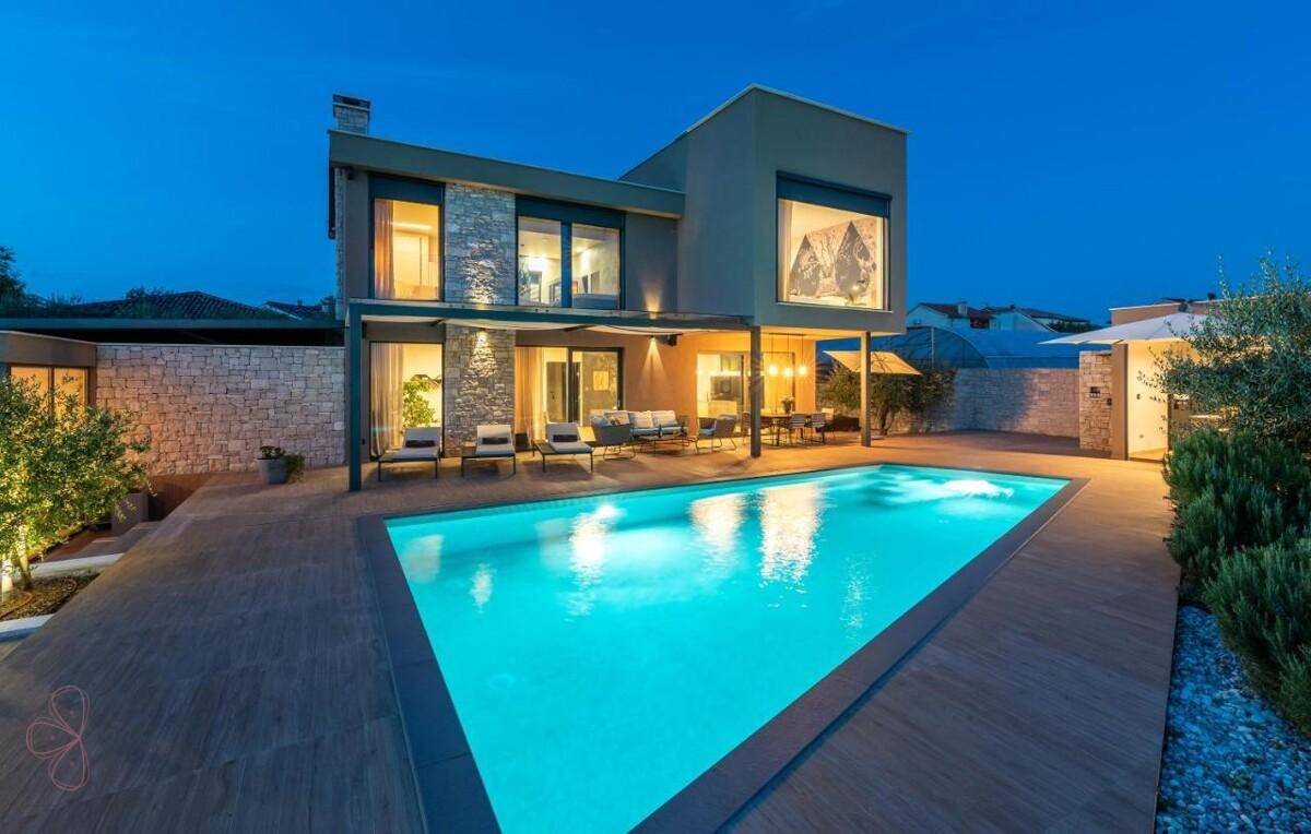 Elegante Villa mit beleuchtetem Pool und Terrasse bei Nacht, umgeben von mediterraner Vegetation.