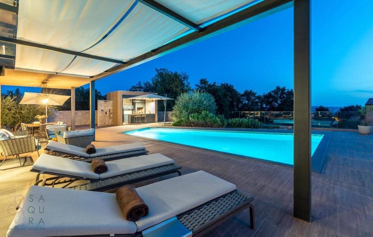 Überdachte Terrasse mit bequemen Liegestühlen und Blick auf den beleuchteten Pool bei Nacht.