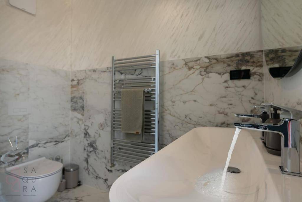 Helles Badezimmer mit Marmorfliesen, Einzelwaschbecken, beheiztem Handtuchhalter und wandhängendem WC.