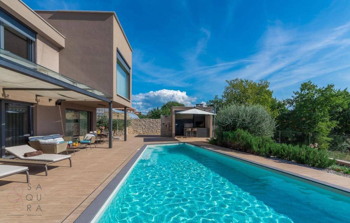 Moderne Villa mit großem Pool, Liegestühlen und gepflegtem Garten unter blauem Himmel.