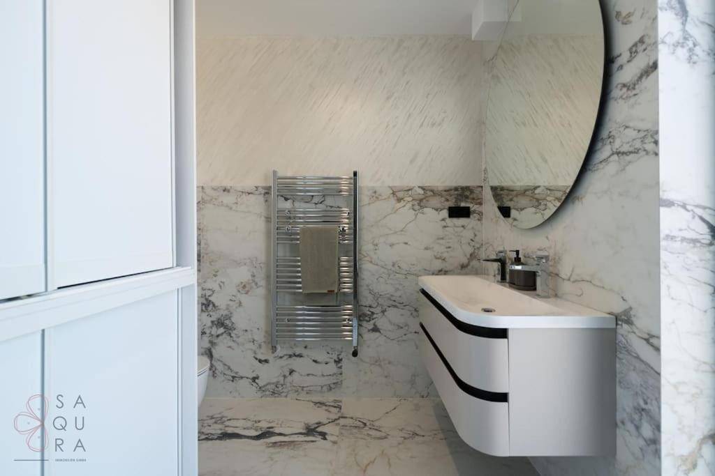Modernes Badezimmer mit Marmorwänden, schwebendem Waschtisch, beheiztem Handtuchhalter und rundem Spiegel.