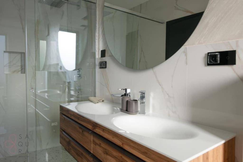Elegantes Badezimmer mit Marmorfliesen, Doppelwaschbecken auf Holzunterschrank und begehbarer Dusche.