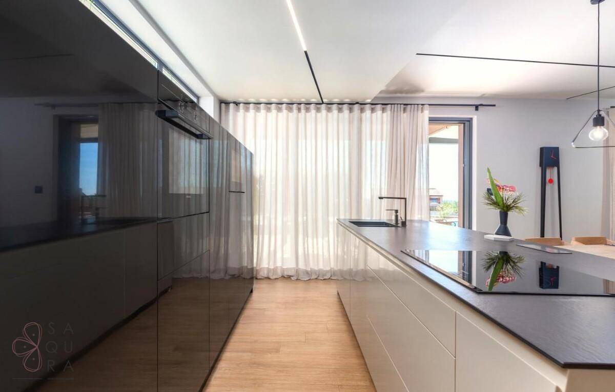 Elegante moderne Küche mit dunklen Hochglanzfronten, Kochinsel und viel Tageslicht.