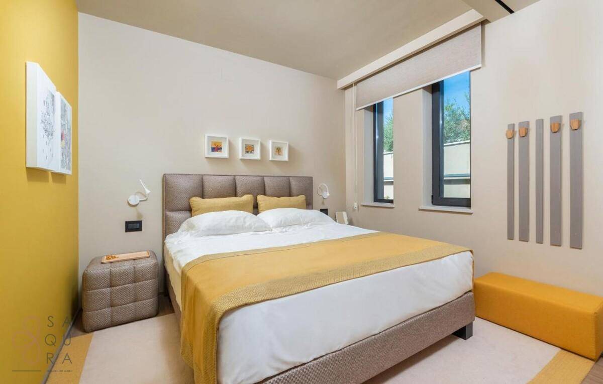 Gemütliches Schlafzimmer mit Doppelbett, gelben Akzenten und natürlichem Lichteinfall.