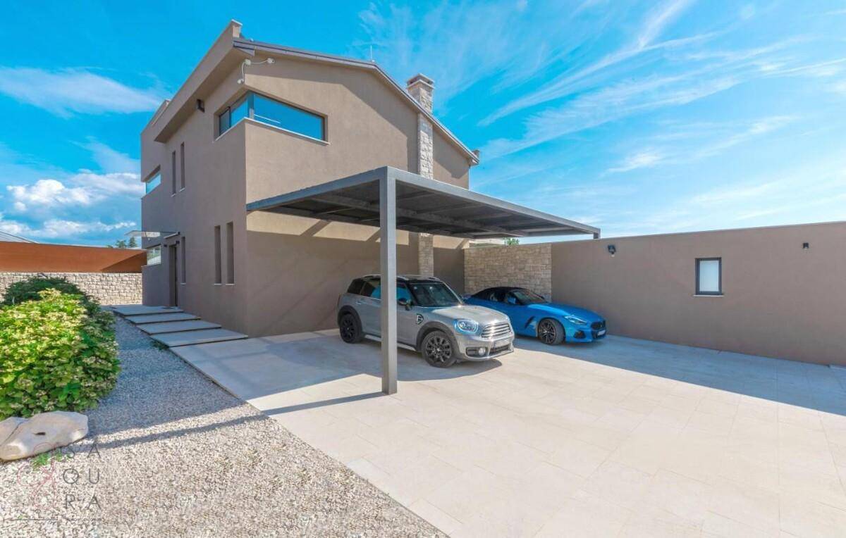 Moderne Villa mit Carport für zwei Fahrzeuge und gepflegter Zufahrt unter blauem Himmel.