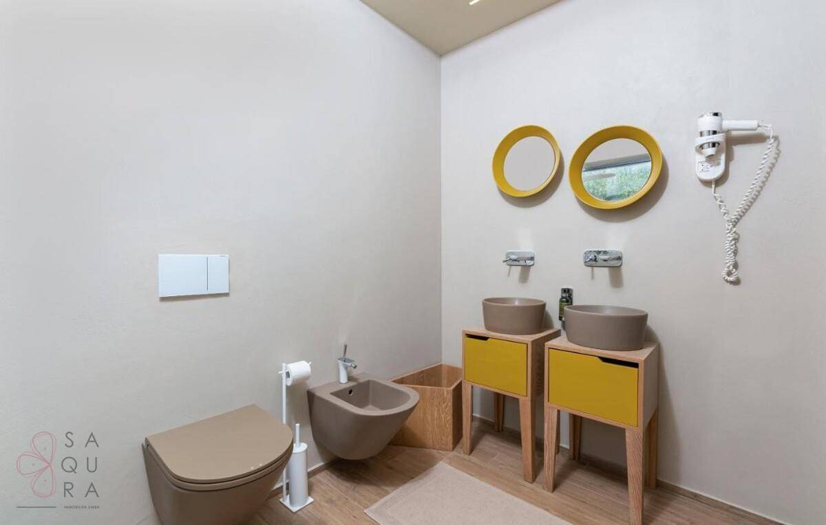 Modernes Badezimmer mit Doppelwaschbecken, Toilette, Bidet und farbigen Akzenten.