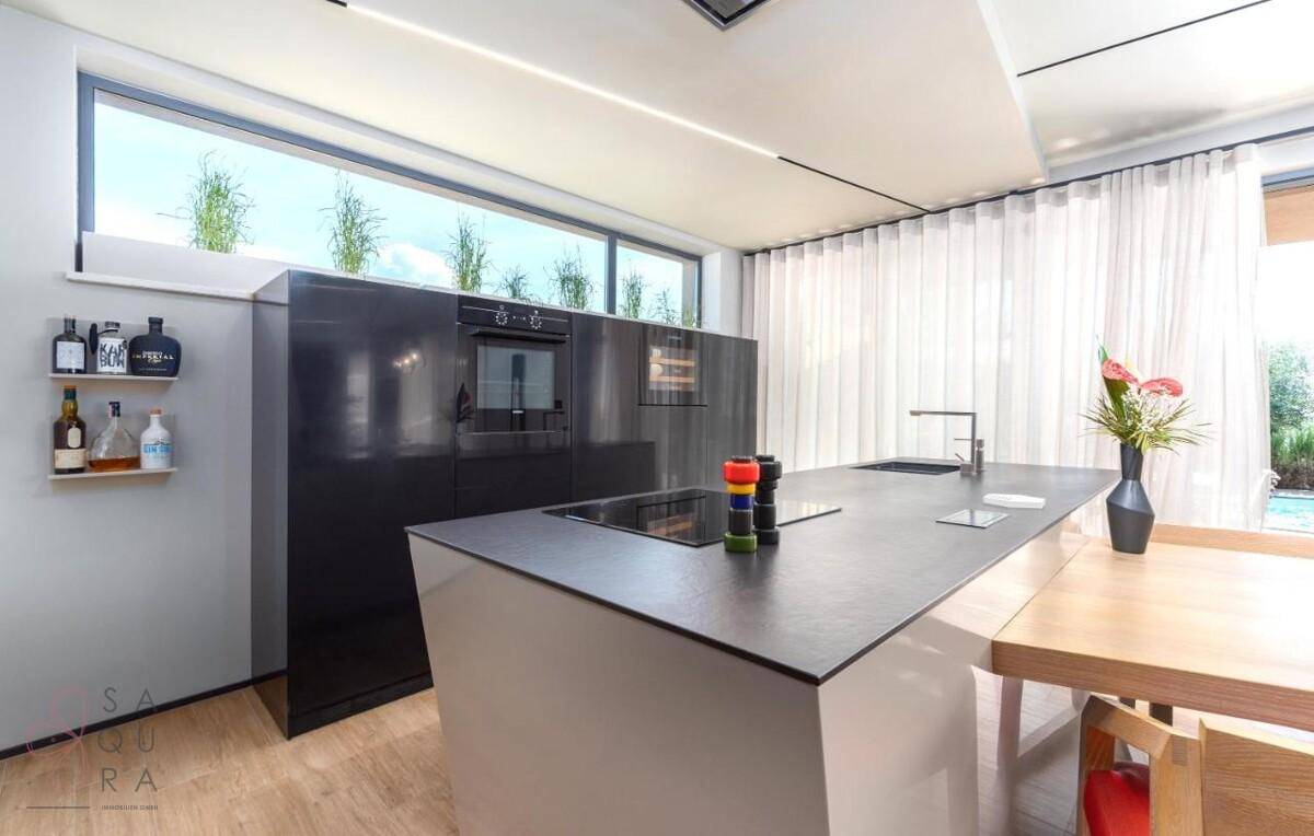 Moderne Küche mit schwarzer Kücheninsel, integrierten Geräten und großem Fenster.