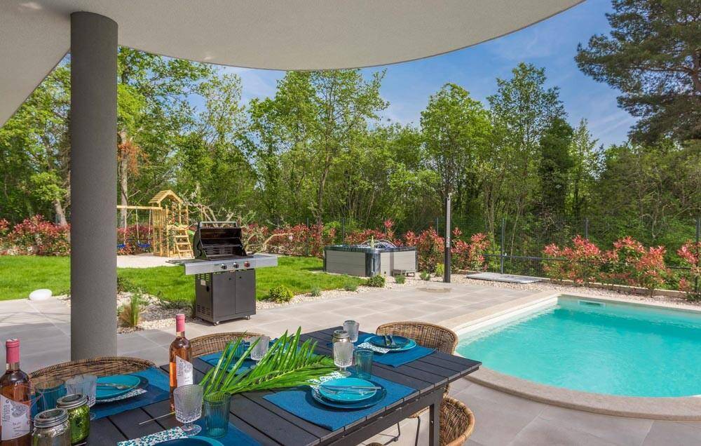 Überdachter Essbereich im Freien mit Grill, Blick auf den Pool, Whirlpool und Kinderspielplatz.