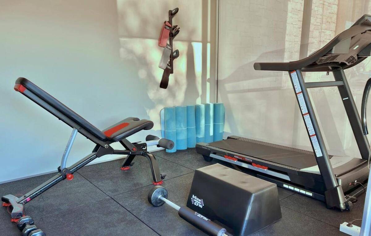 Gut ausgestatteter Fitnessraum mit Laufband, Hantelbank und weiteren Trainingsgeräten.