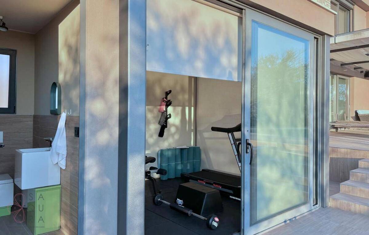 Fitnessraum mit Trainingsgeräten und Zugang zur Terrasse durch große Glasschiebetüren.