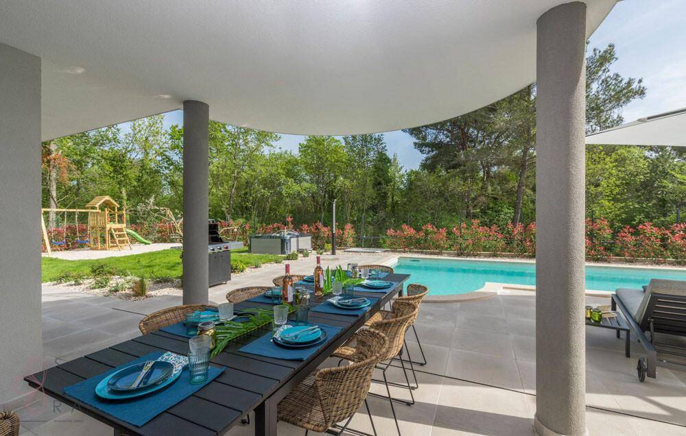 Eleganter überdachter Essbereich im Freien mit Blick auf den Pool und die grüne Gartenlandschaft.