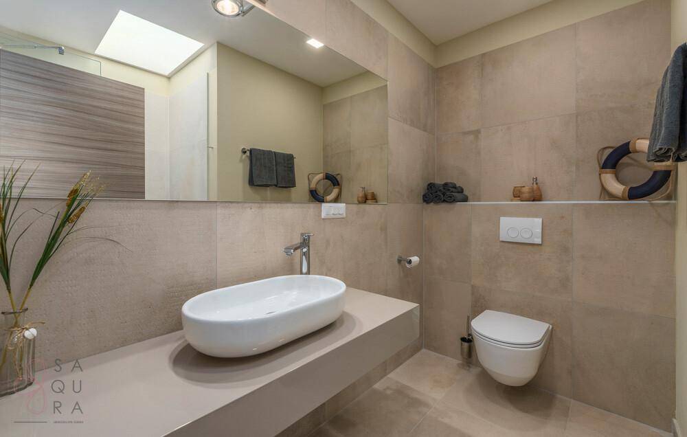 Modernes Badezimmer mit Einzelwaschbecken, wandhängendem WC und natürlichem Licht durch Oberlicht.