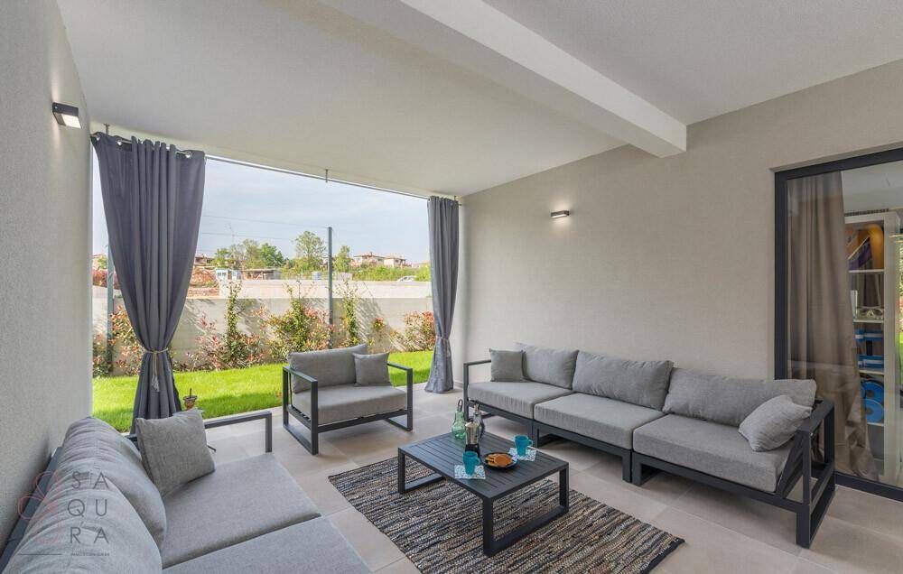 Gemütlicher überdachter Loungebereich im Freien mit modernen Sofas und Blick auf den Garten.