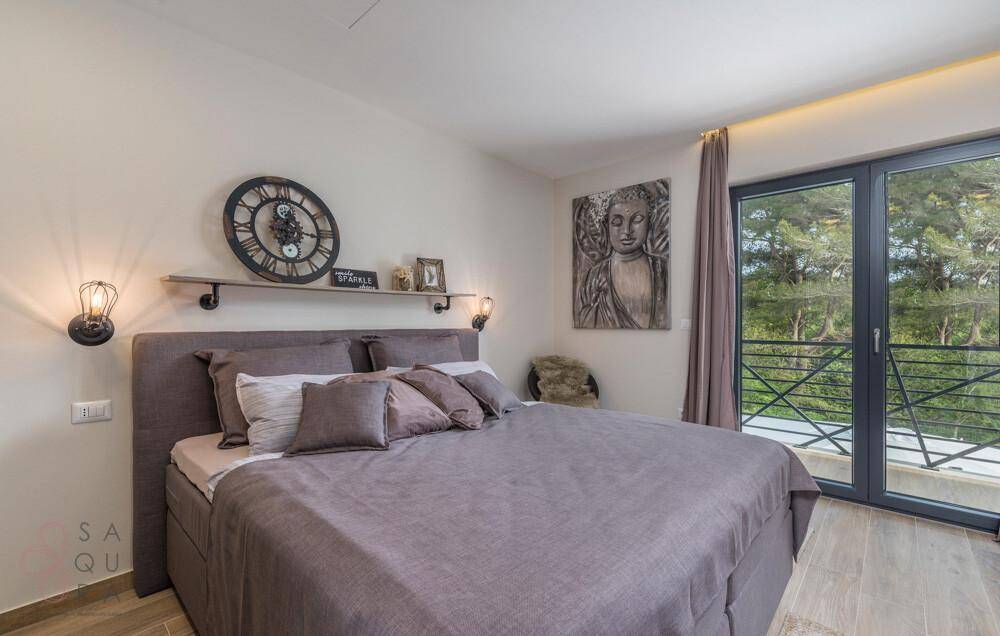 Stilvolles Schlafzimmer mit großem Bett, dekorativer Wanduhr und Balkonzugang mit Waldblick.