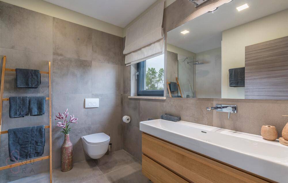 Modernes Badezimmer mit großformatigen Fliesen, Einzelwaschbecken und Fenster für Tageslicht.