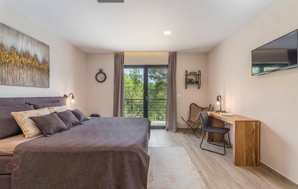 Helles Schlafzimmer mit großem Bett, Holzschreibtisch und Balkonzugang mit Blick ins Grüne.