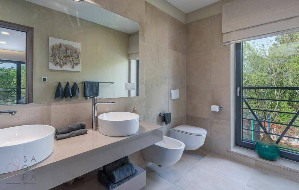Modernes Badezimmer mit Doppelwaschbecken, Bidet und großem Fenster mit Blick ins Grüne.