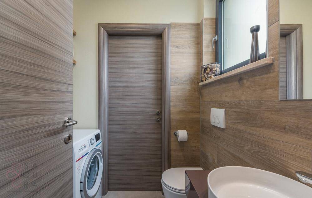 Kleines Badezimmer mit Waschmaschine, Waschbecken und Holzverkleidung an den Wänden.