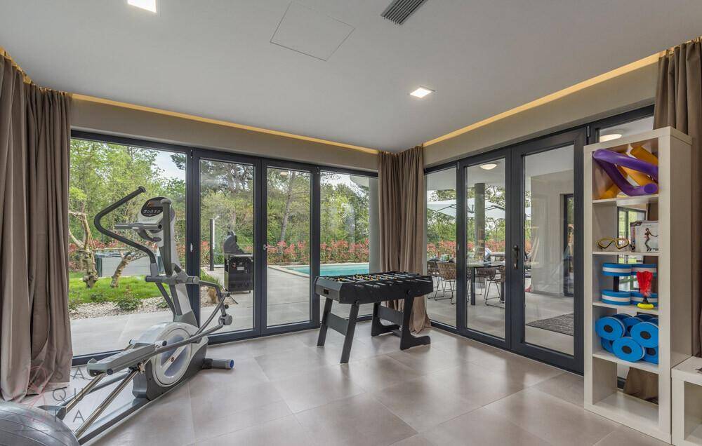 Geräumiges Fitnesszimmer mit Trainingsgeräten, Tischfußball und Zugang zum Poolbereich.
