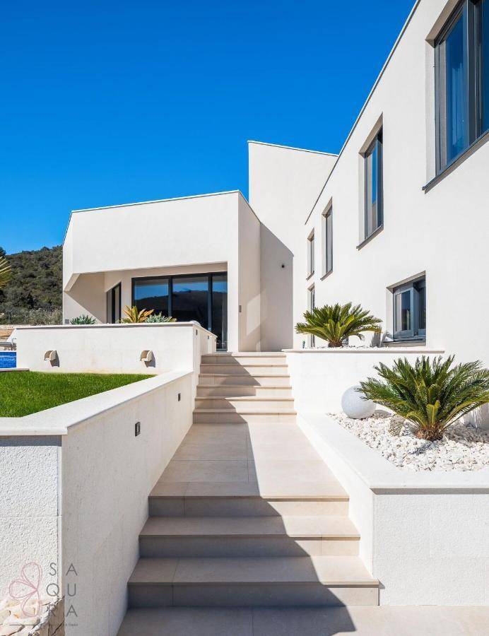 Elegante Außentreppe führt zum Eingang der modernen Villa mit minimalistischer Architektur und mediterraner Bepflanzung.