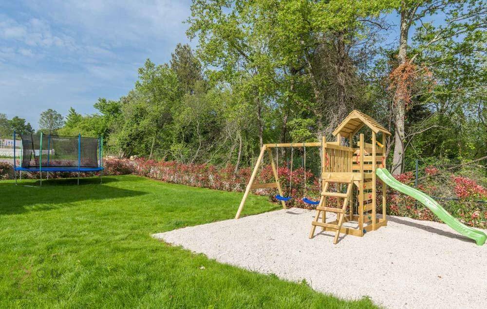 Großer Kinderspielplatz mit Schaukeln, Rutsche und Trampolin auf einer weitläufigen Rasenfläche.