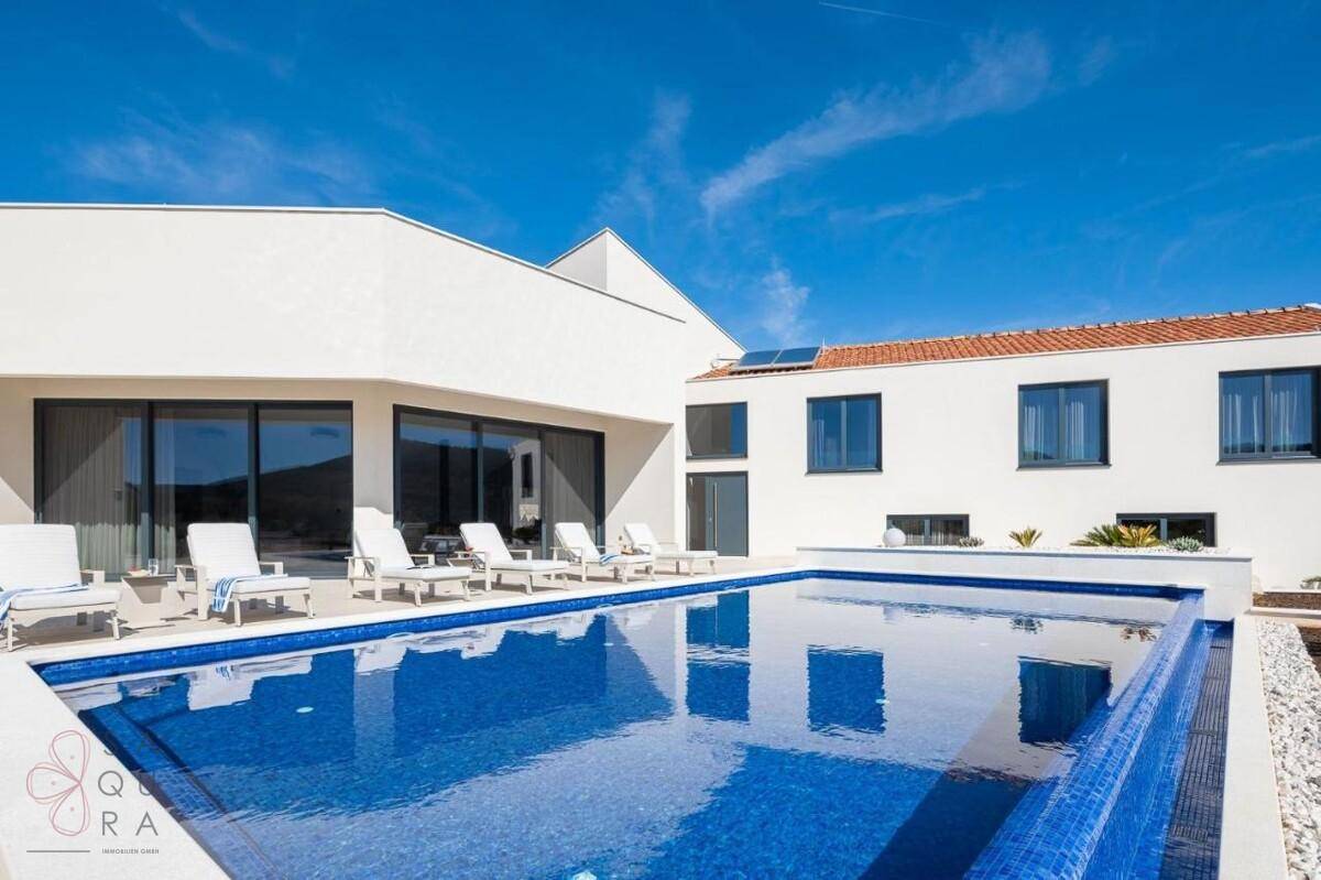 Großzügiger Poolbereich mit blauen Mosaikfliesen und bequemen Liegestühlen vor der modernen Villa.
