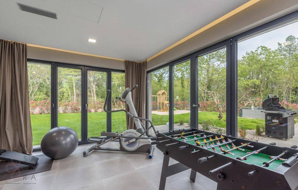 Fitness- und Spielzimmer mit Trainingsgeräten, Tischfußball und Blick in den Garten.