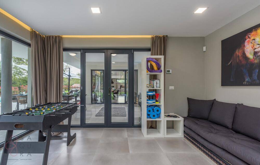 Spielzimmer mit Tischfußball, Sofa und Blick auf den Poolbereich durch große Fenster.