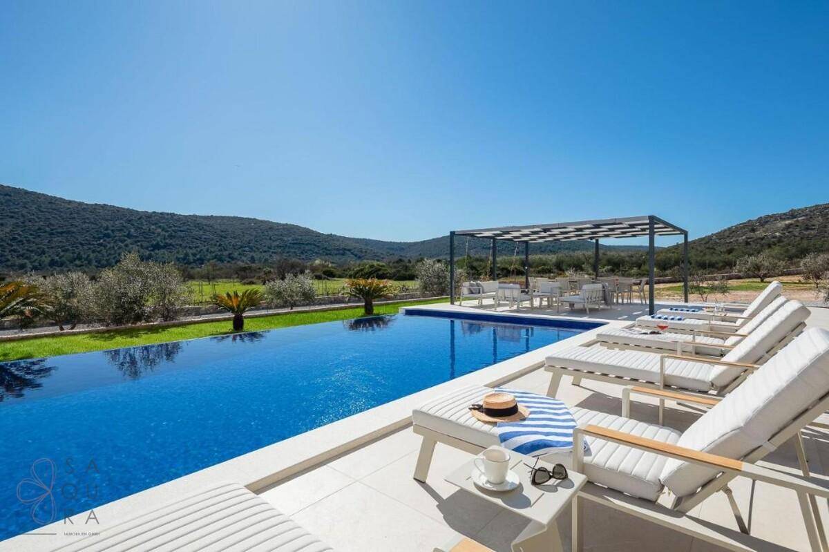 Atemberaubender Infinity-Pool mit bequemen Liegestühlen und weitem Blick über die hügelige Landschaft.