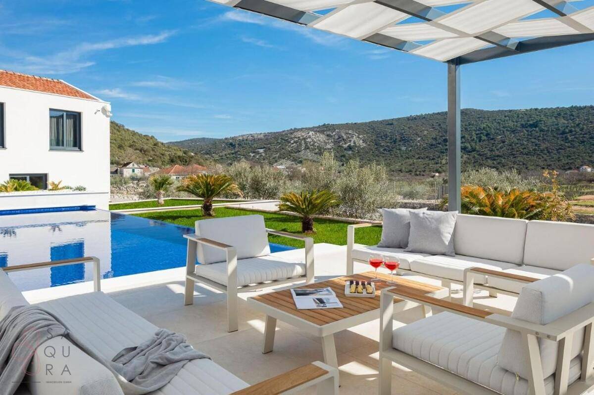 Komfortabler Lounge-Bereich im Freien unter einer Pergola, direkt am Pool mit Panoramablick.