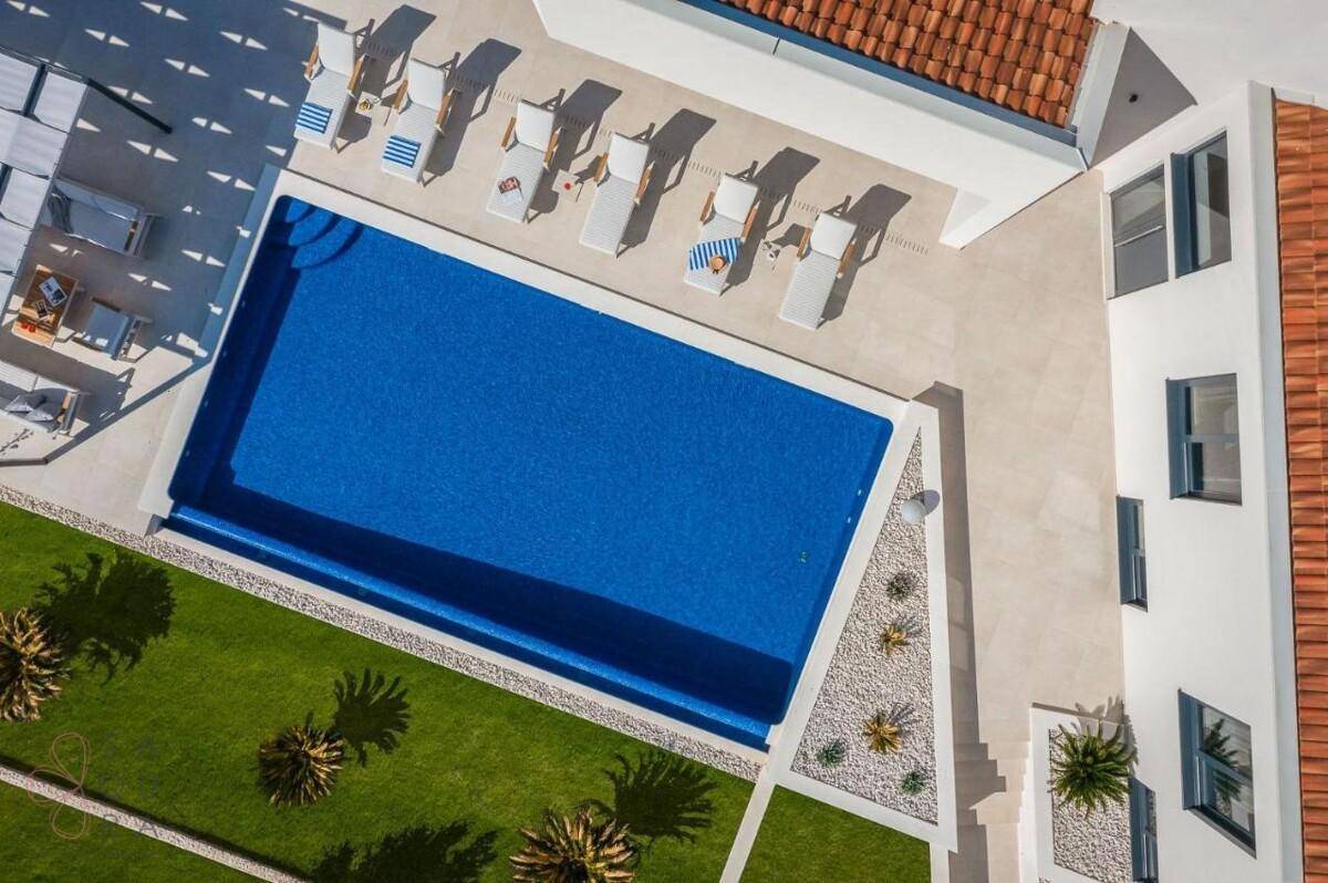 Vogelperspektive des rechteckigen Pools mit Liegestühlen und gepflegtem Rasenbereich der Villa.