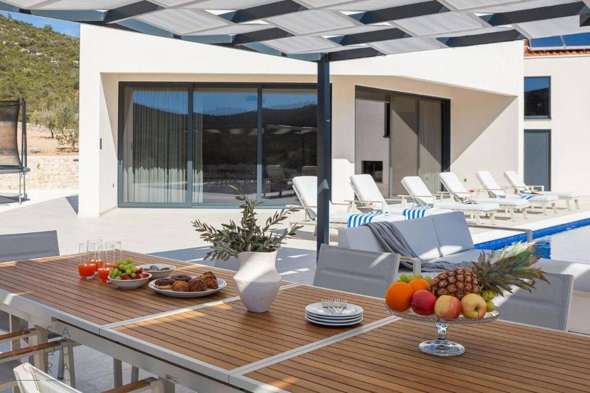 Großer Esstisch im Freien unter einer Pergola, ideal für Mahlzeiten mit Blick auf den Pool und die Natur.