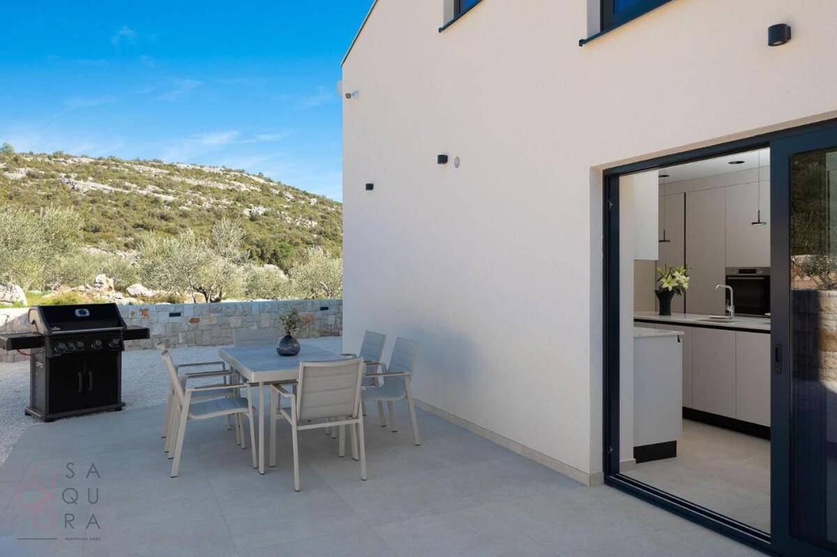 Gemütliche Terrasse mit Grillbereich und Esstisch, direktem Zugang zur Küche und Blick auf die Landschaft.