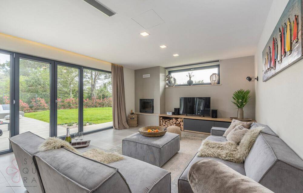 Gemütliches Wohnzimmer mit modernem Sofa, Kamin und großen Fenstern zum Garten.