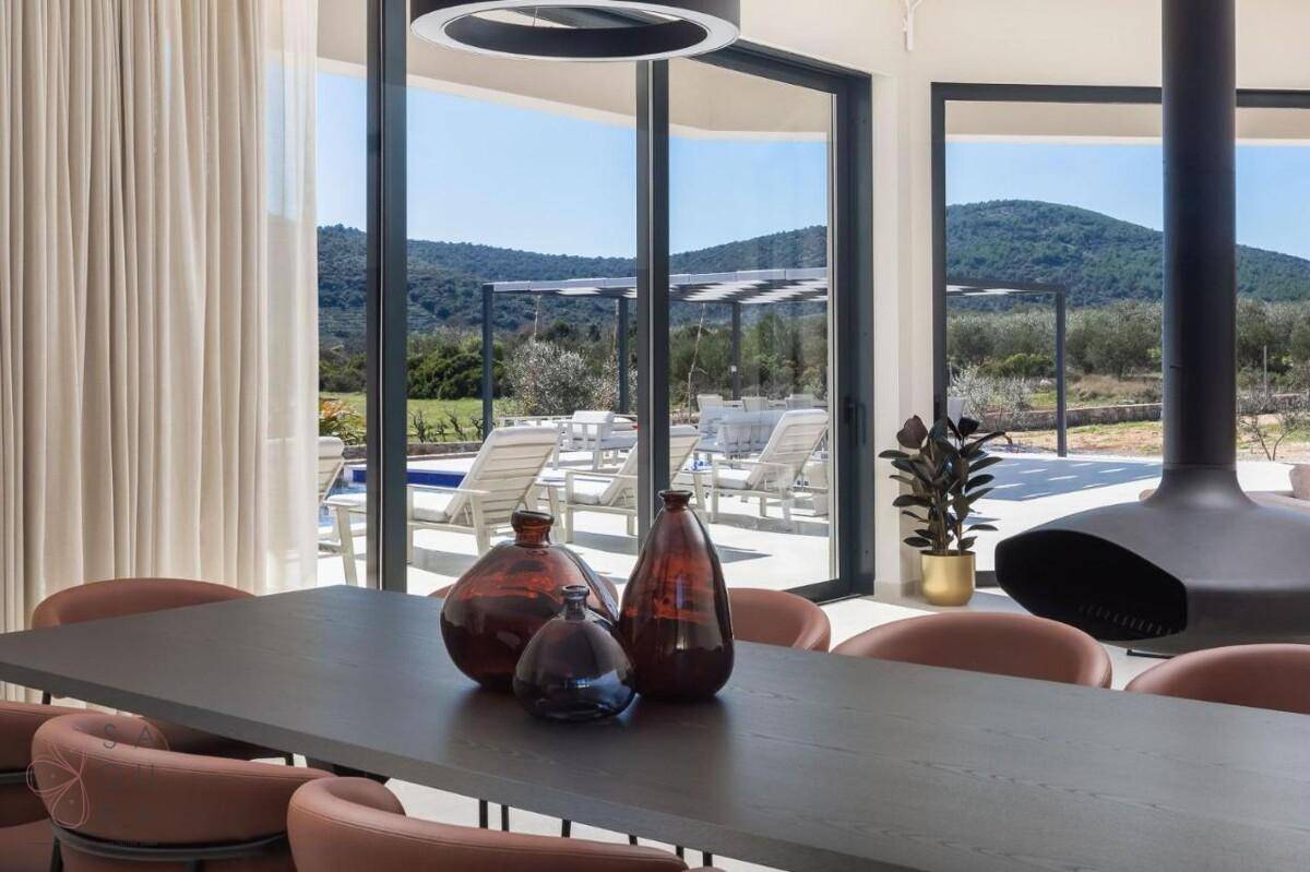 Eleganter Essbereich mit großem Tisch, Hängekamin und weitem Blick durch bodentiefe Fenster auf die Landschaft.