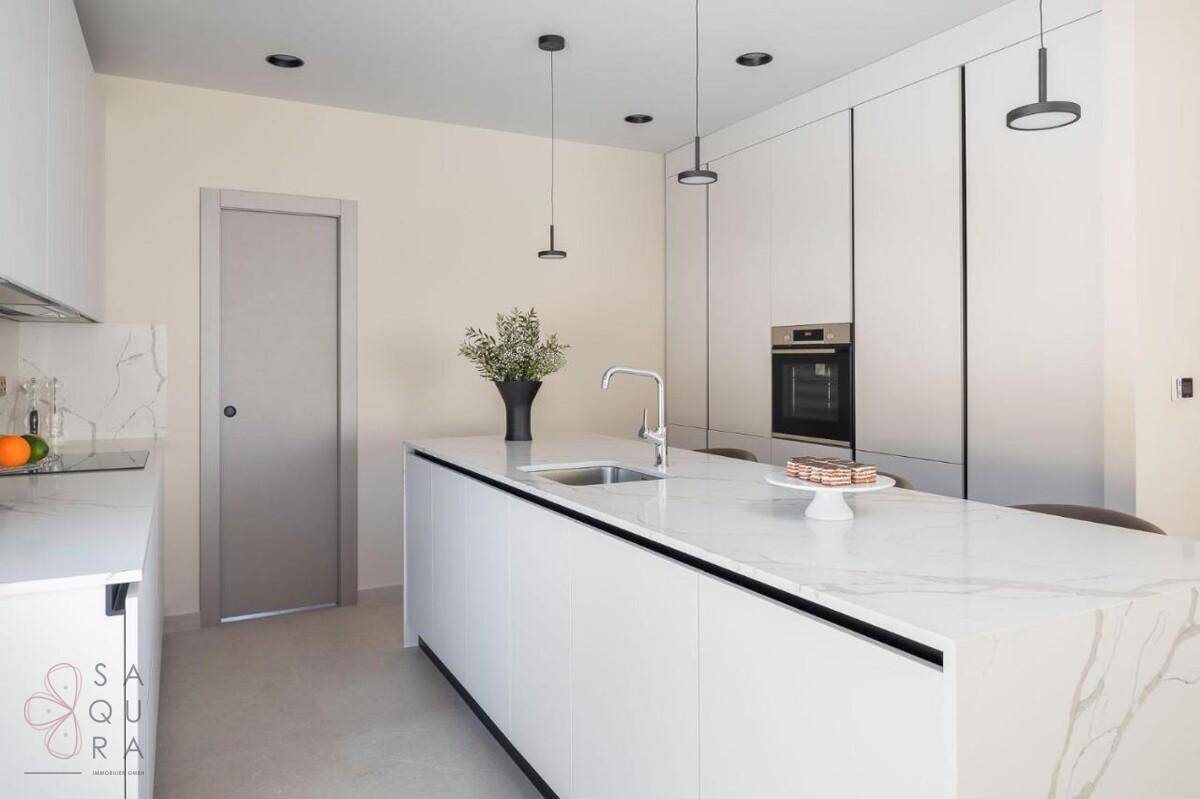 Moderne Küche mit weißer Kücheninsel, integrierten Geräten und eleganten Marmor-Arbeitsplatten.